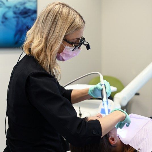 Une dentiste aux loupes éclairées traite une patiente.