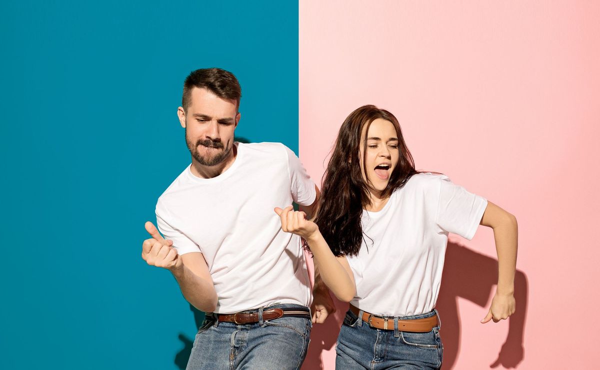 Un homme et une femme en t-shirt blanc dansent devant un mur mi-turquoise, mi-rose.